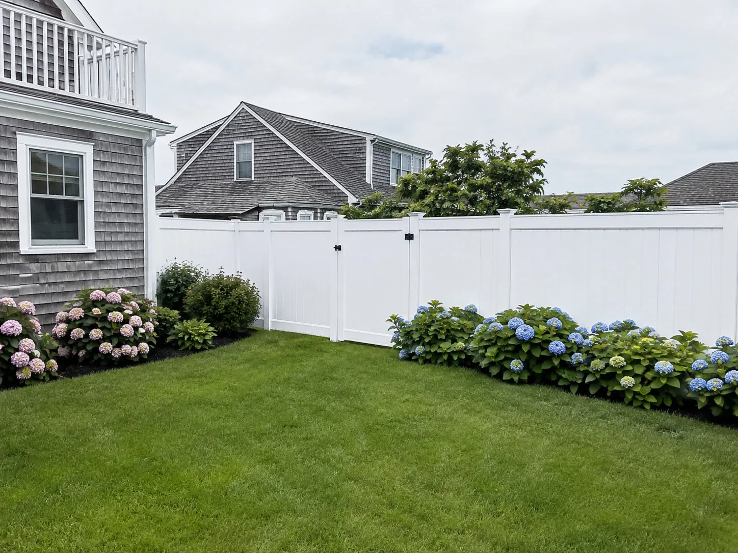 White vinyl privacy fence with a matching gate enclosing a landscaped backyard in Plymouth, MA